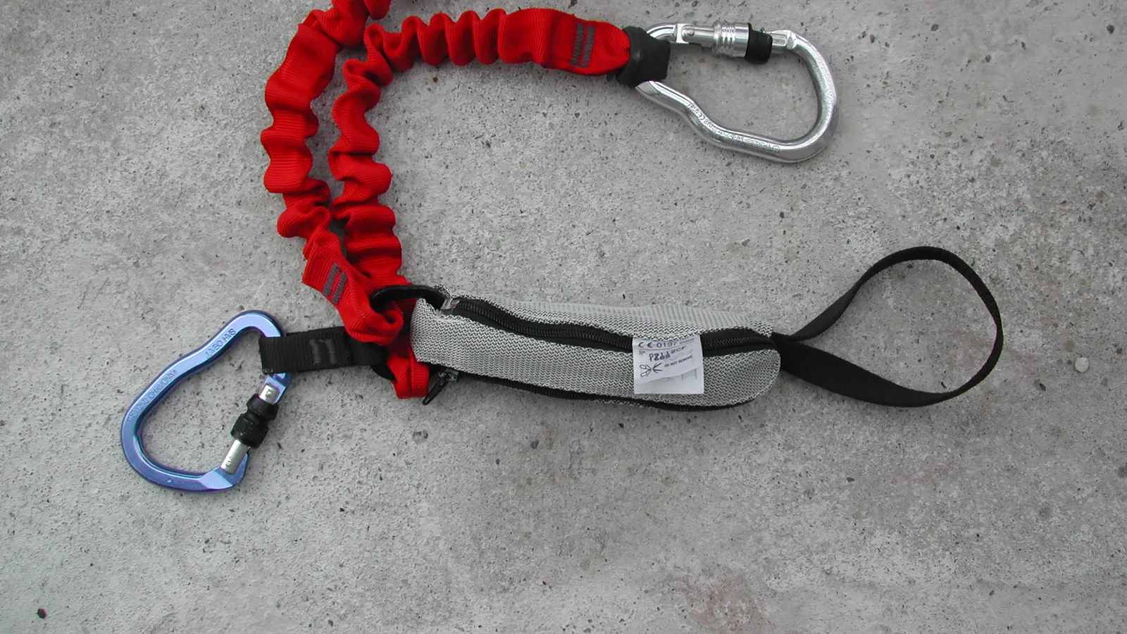 A climbing safety lanyard with two locking carabiners and an energy absorber on concrete