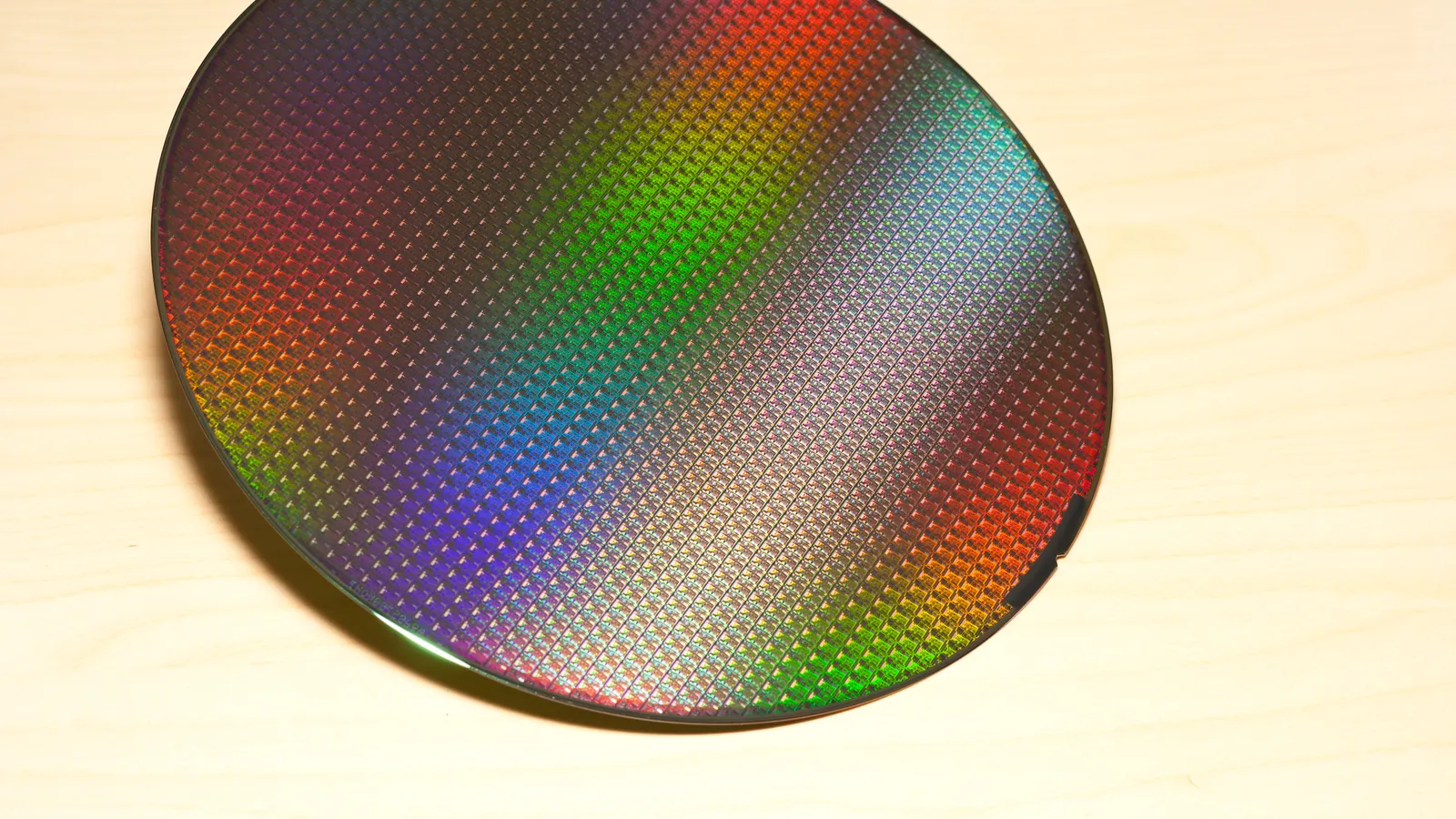 A patterned silicon wafer reflecting rainbow colors across its grid of chips