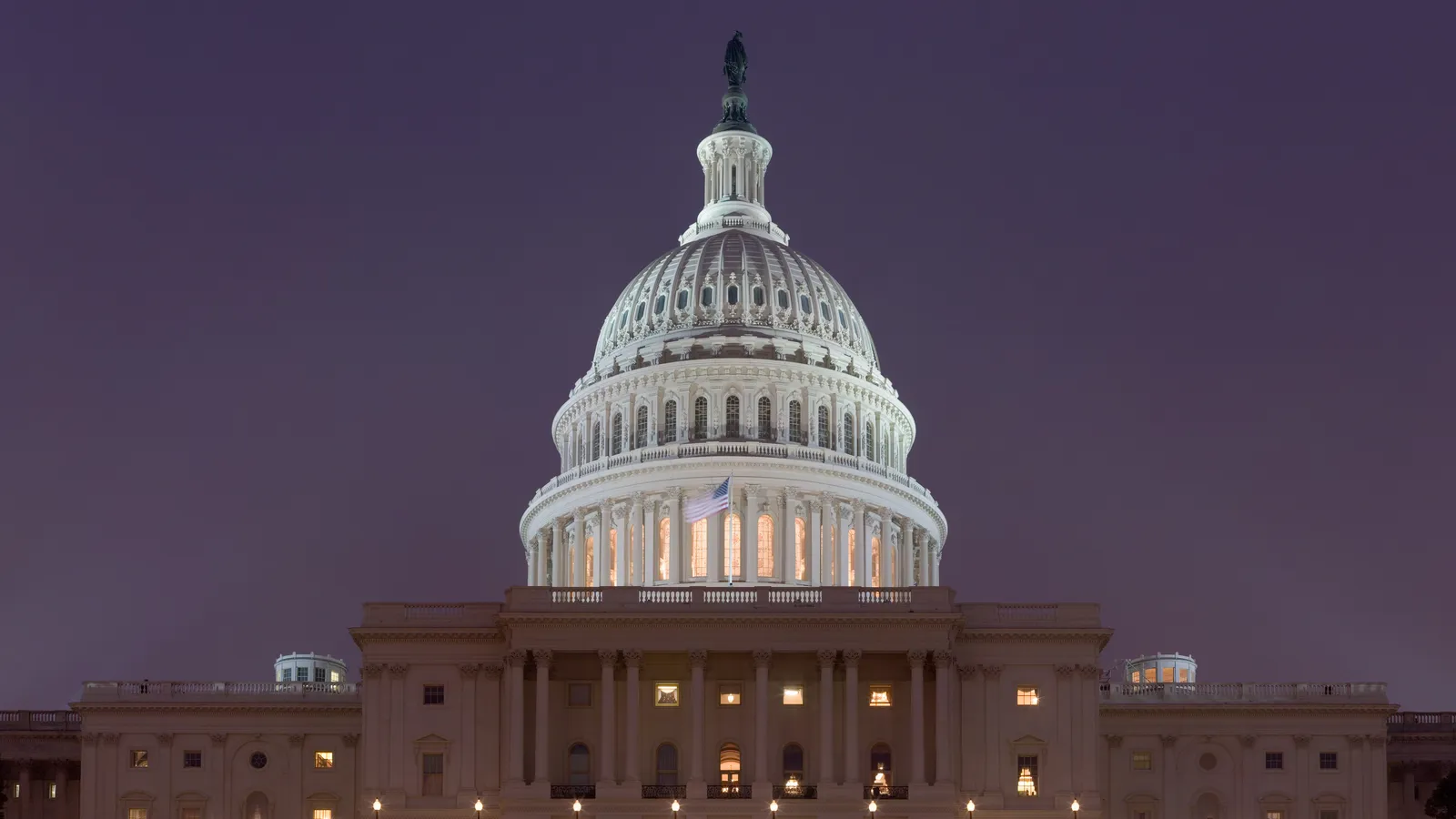 The United States Capitol building lit up at night, dome glowing against a dusk sky.